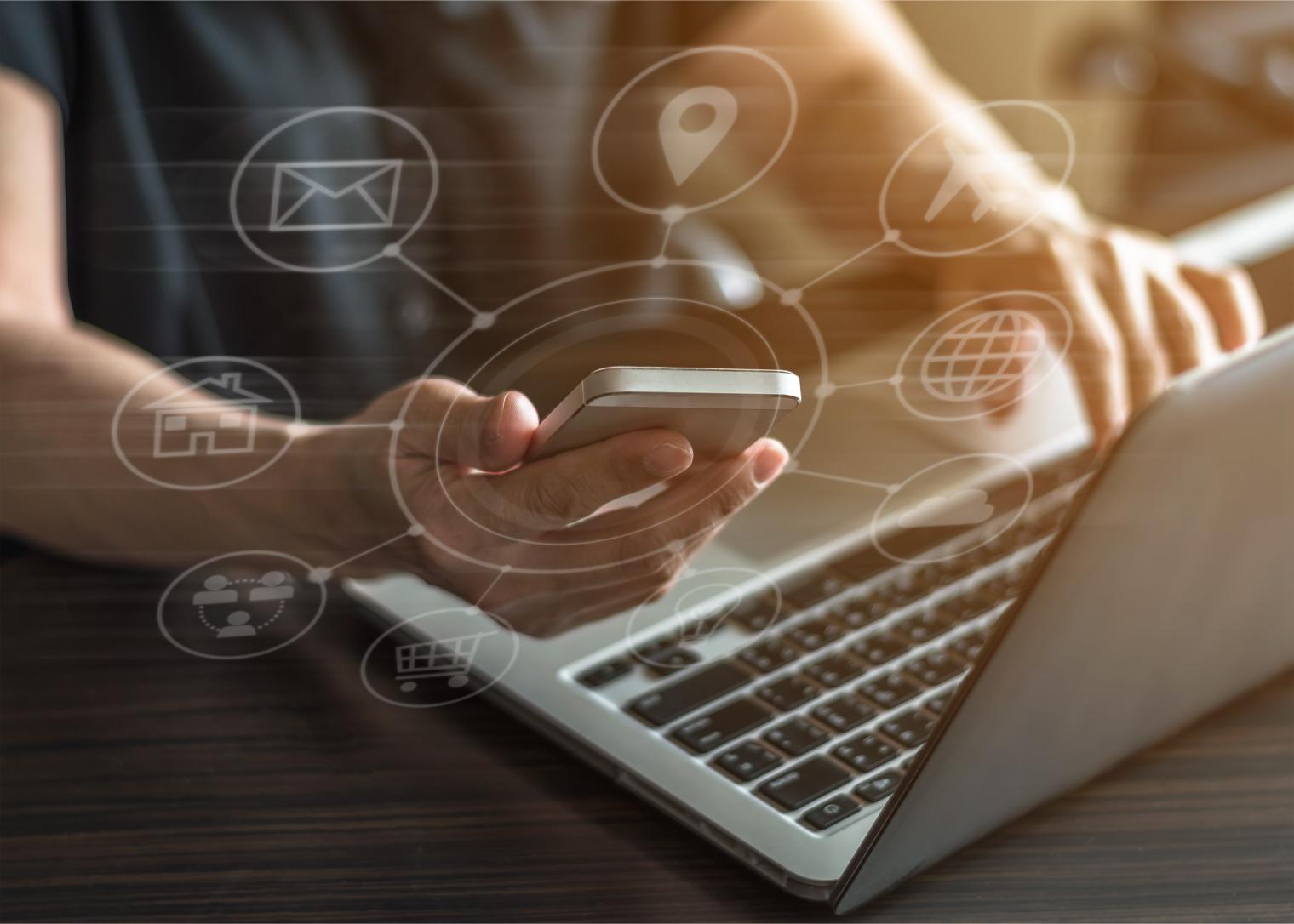 Person working on laptop while holding phone